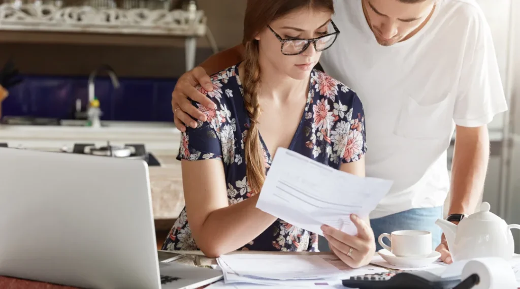 A young couple collaborates on their finances, reviewing documents and discussing options for borrowing during a consumer proposal.