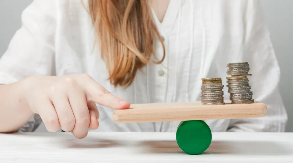 Une femme tenant une pile de pièces sur une balance en bois, symbolisant la gestion financière d'un syndic de faillite.