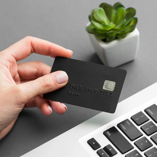 A hand holds a credit card beside a laptop, symbolizing online payments and debt management.