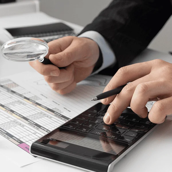 A man in a suit uses a calculator and magnifying glass, focused on his calculations.