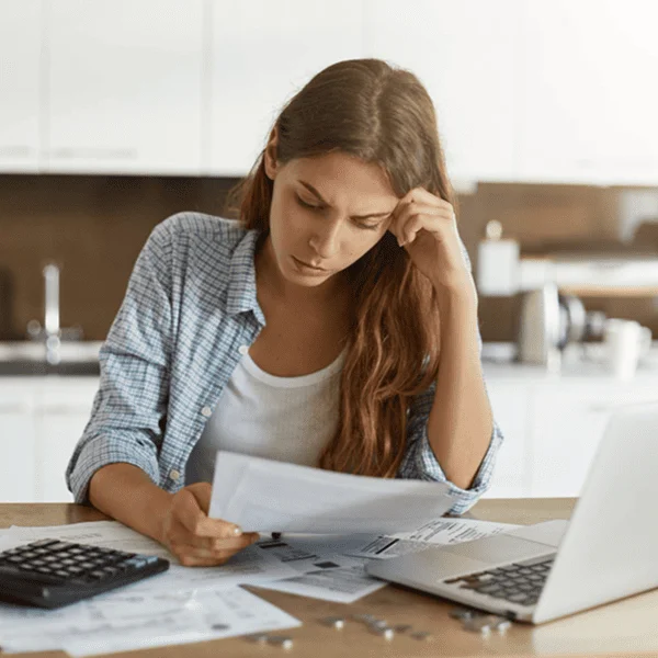Woman working on a laptop with paperwork spread out on a desk, focused on her tasks.