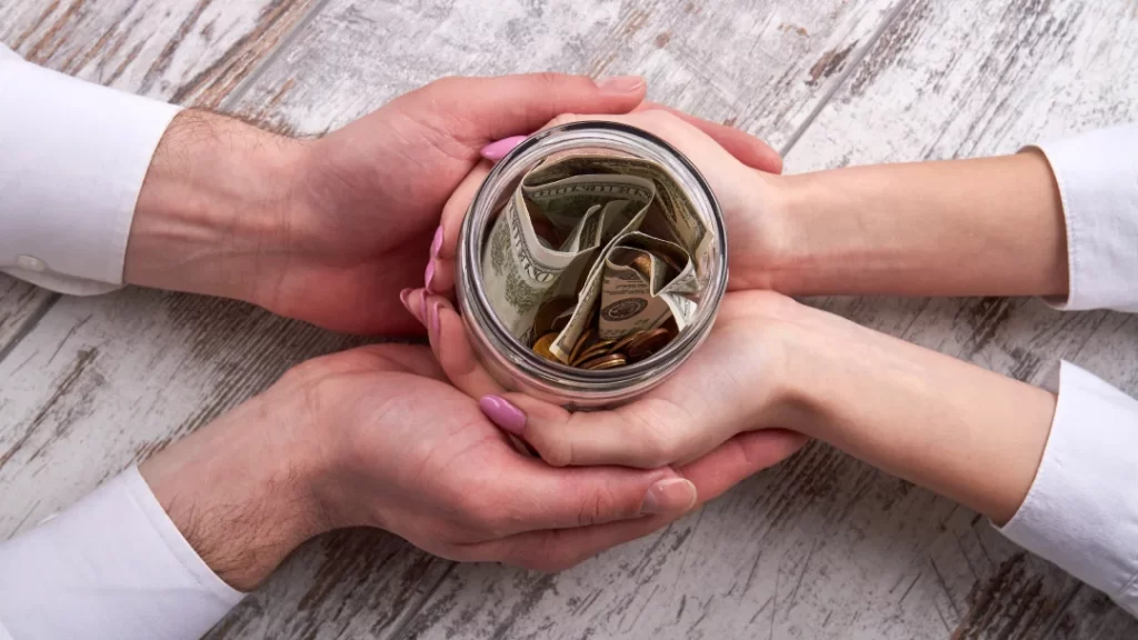 Hands grasping a jar filled with coins, symbolizing savings and financial growth.