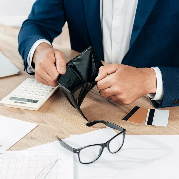 A man in a suit holds an empty wallet, conveying a sense of financial struggle or disappointment.