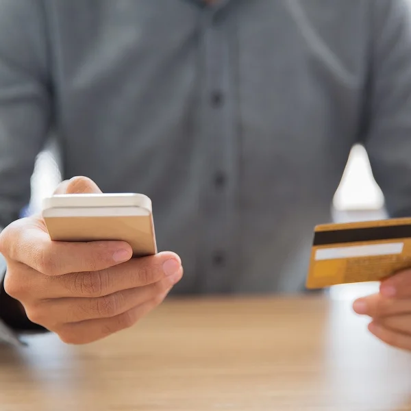 Man holding a credit card in one hand and a mobile phone in the other, appearing to make a transaction.