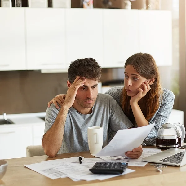 Couple reviewing paperwork together at a kitchen table, surrounded by homey decor and natural light.