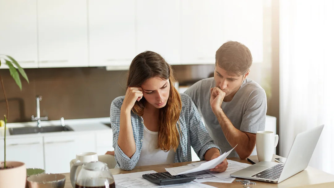 A man and woman sit at a table with a laptop and papers, engaged in discussion or collaboration.