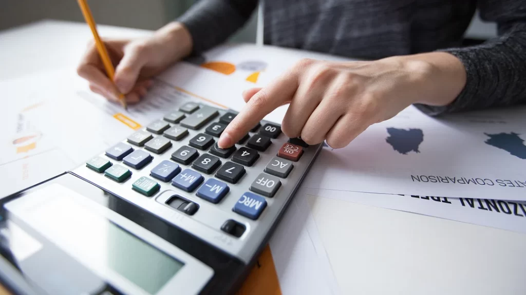 A person focused on calculations while using a handheld calculator on a desk.