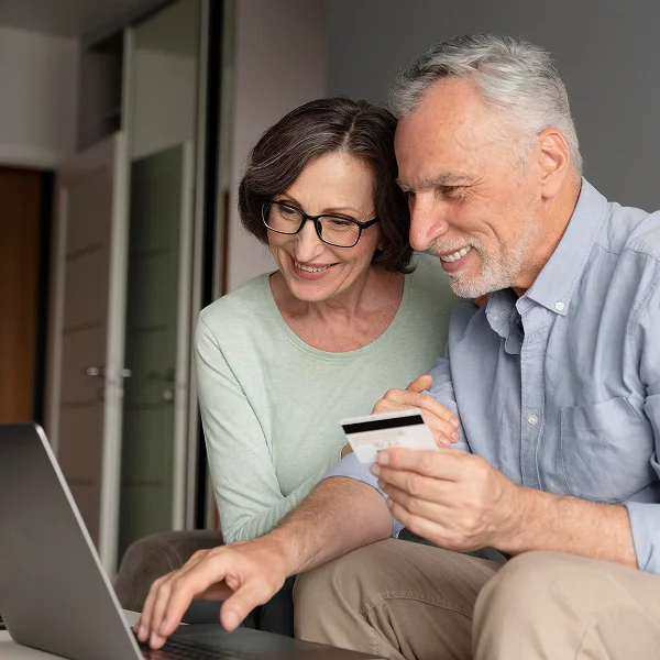 An older couple sitting together, using a laptop and a credit card for online shopping or banking.