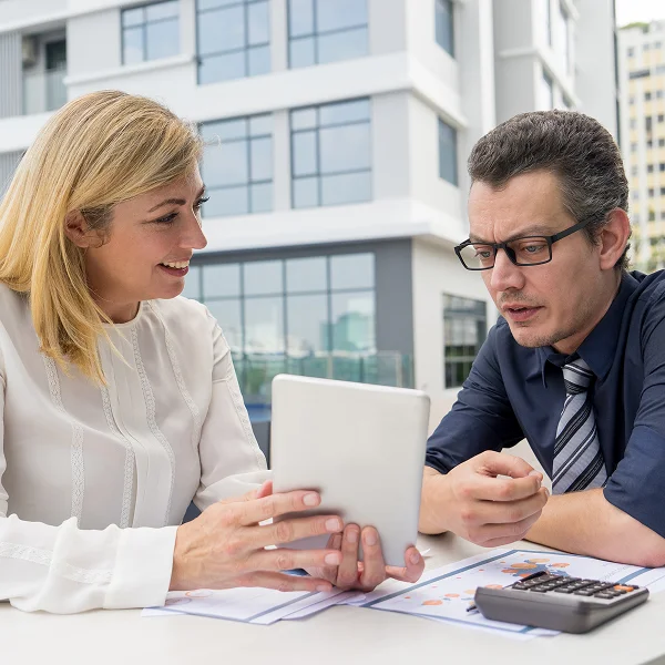 A man and woman sit at a table, engaged with a tablet, discussing or reviewing content together.