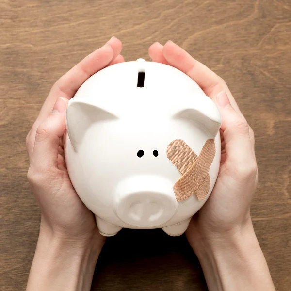 A person holds a bandaged piggy bank, symbolizing financial recovery or the need for saving after setbacks.