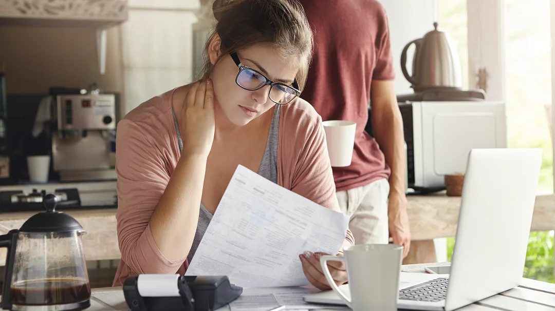 A woman focuses on her laptop while a man stands behind her, observing the screen.