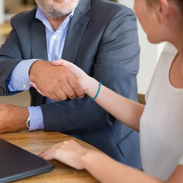 A man and woman shaking hands across a table, symbolizing agreement or partnership.