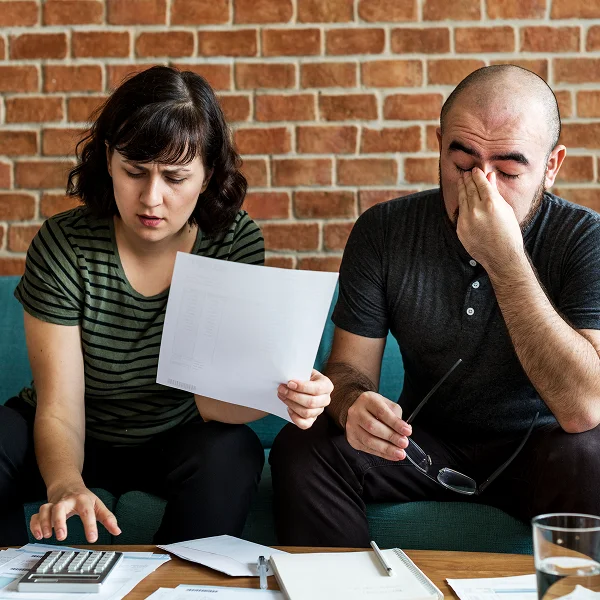 A man and woman sit on a couch, reviewing papers and using a calculator for calculations