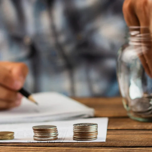Man placing coins into a jar on a wooden table, symbolizing savings for debt consolidation efforts.