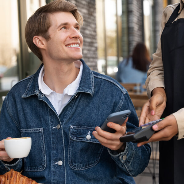 Un homme assis à une table, tenant une tasse de café et un téléphone.